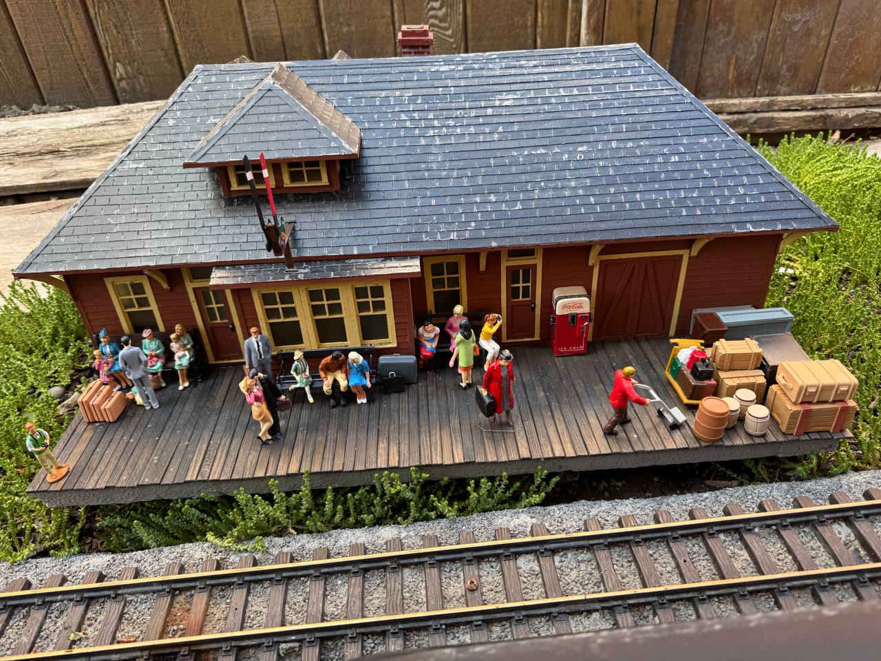 Detailed miniature train station platform with tiny passengers, luggage, and a Coca-Cola vending machine